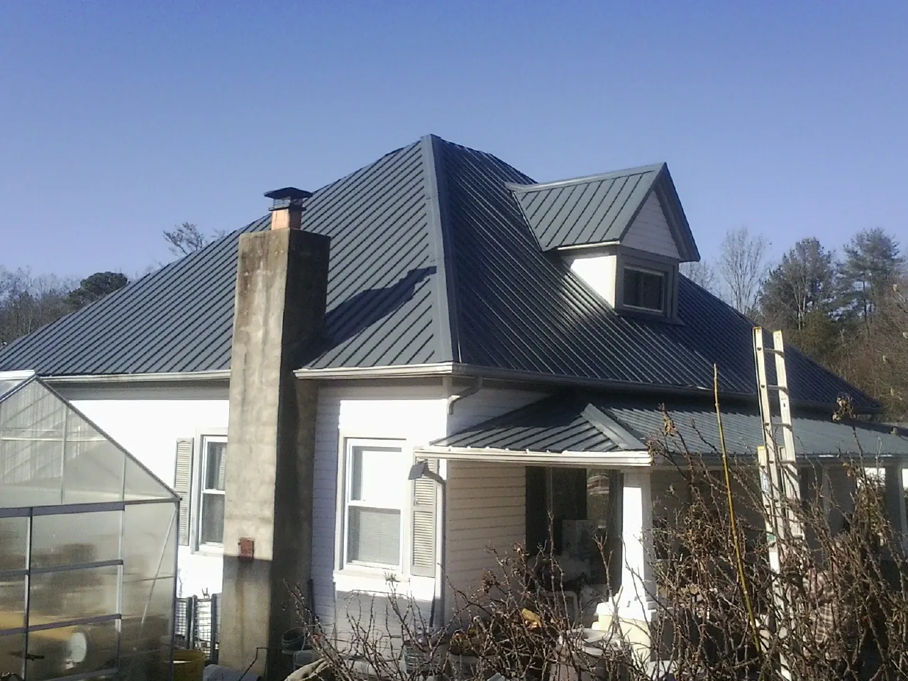 Dark blue standing seam metal roof on a white farmhouse with dormer — Slate & Tile Roof Repair by Roofing Brothers in Vinton