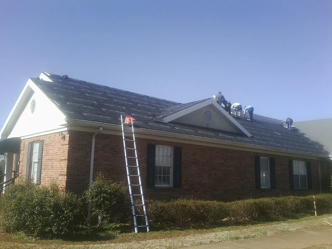 Crew tearing shingles off a brick ranch roof with a ladder set — Emergency Roof Repair work by our crew in Vinton