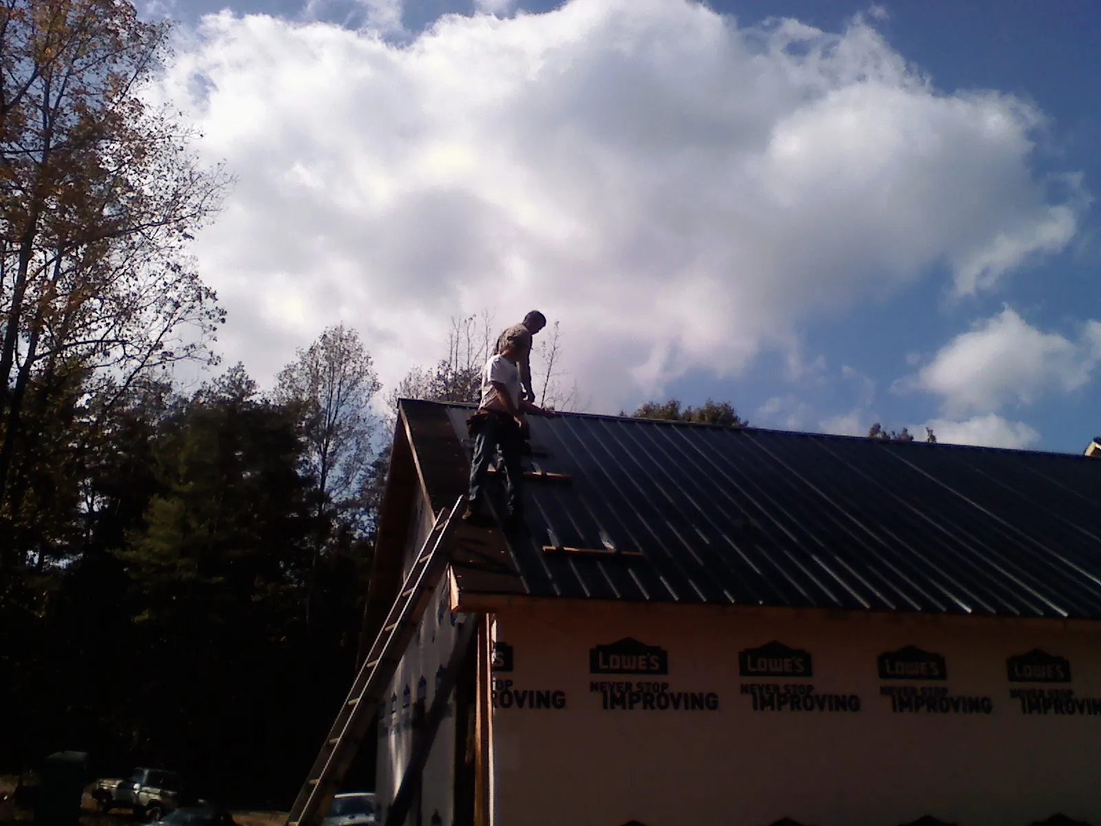 Roofer fastening dark metal panels high against a cloudy sky, from a Roof Inspection job in Vinton